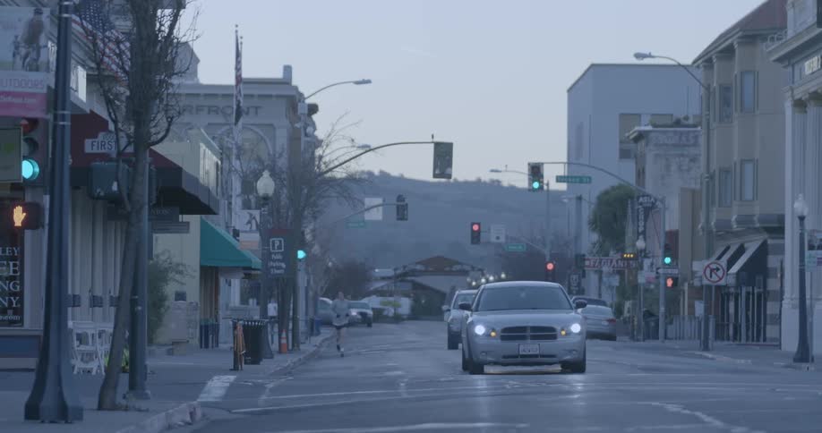 A man jogs down a city road with cars driving past