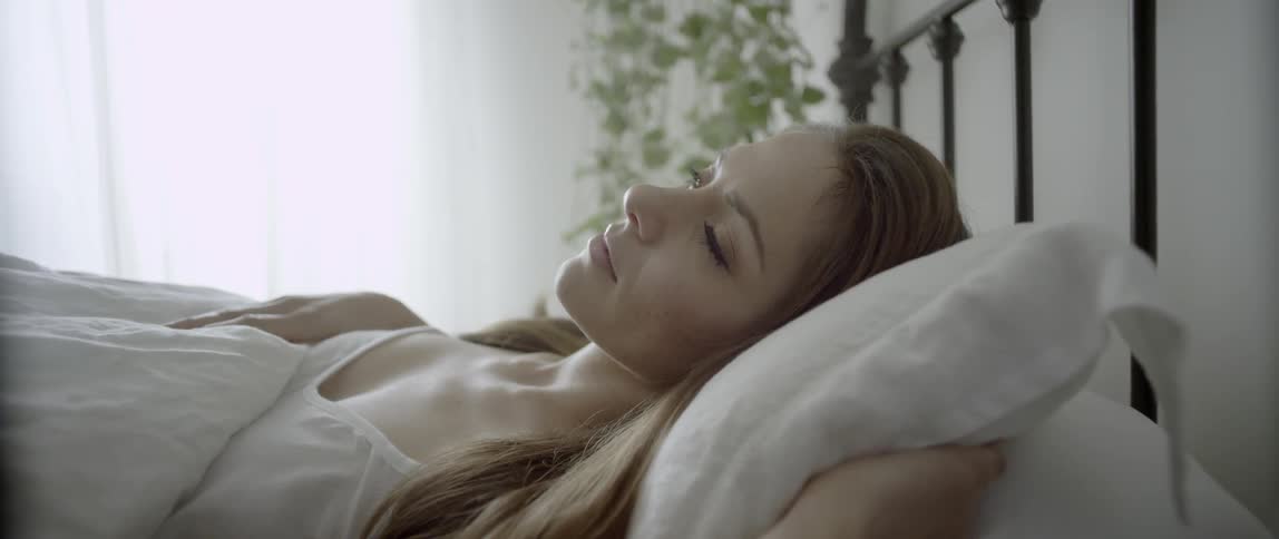 A sleeping woman opens her eyes and looks toward a window