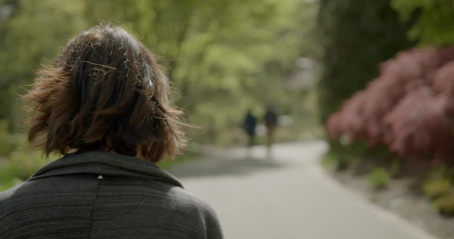 A woman is walking down a wide path through a park