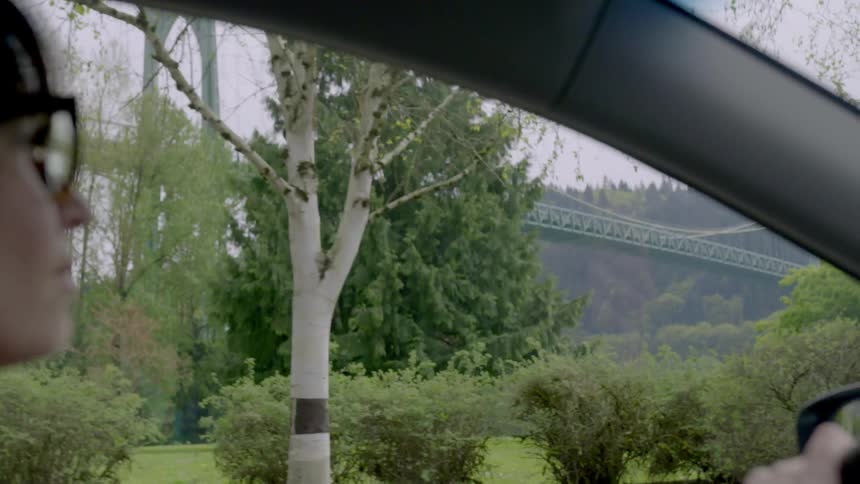 A woman with glasses drives past a bridge