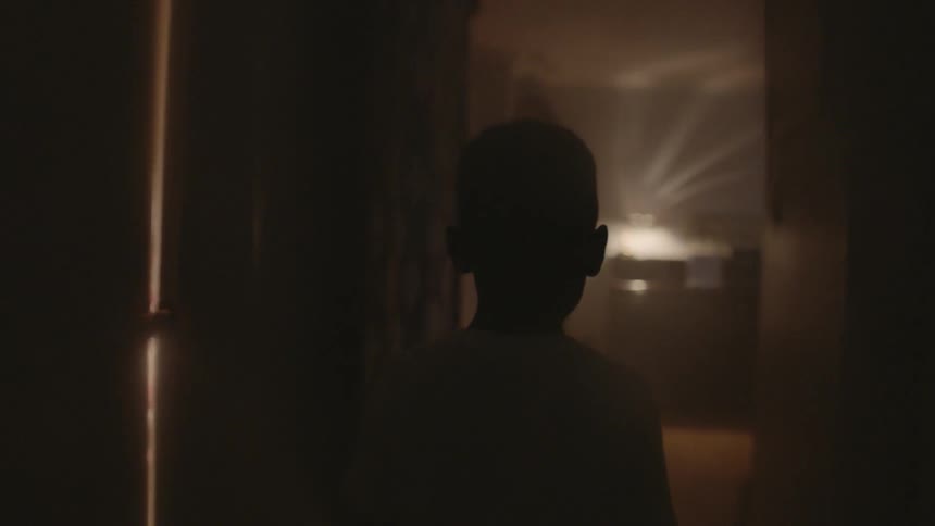 A boy walks down a dimly lit hallway