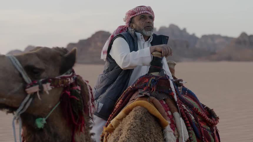 A man is sitting on top of his camel smoking