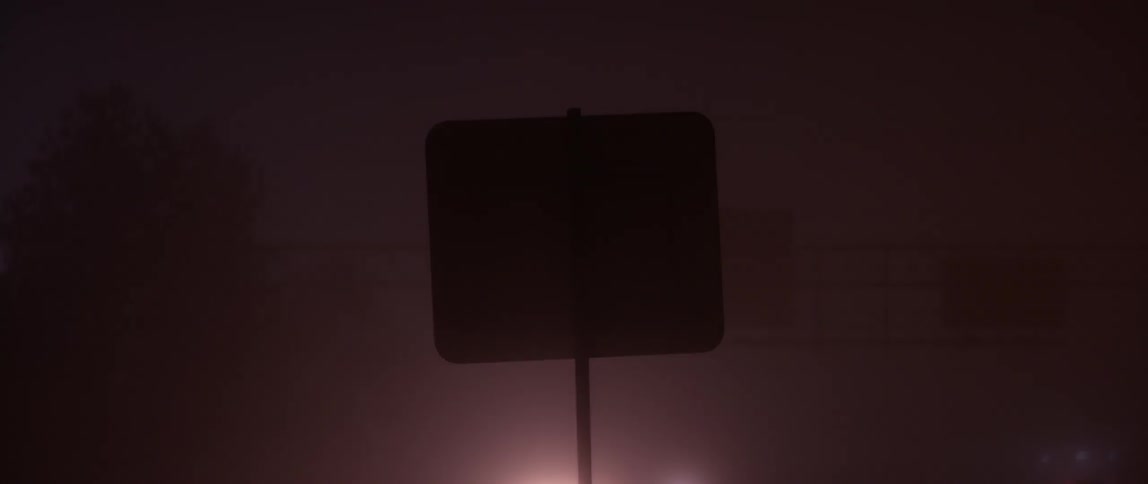 A truck and car are driving past a sign in foggy weather