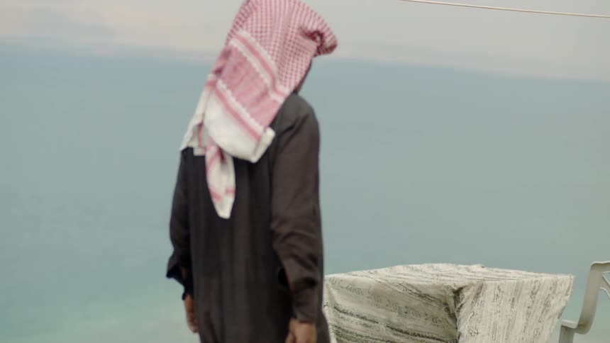 An arab man is walking towards a table in a desert landscape