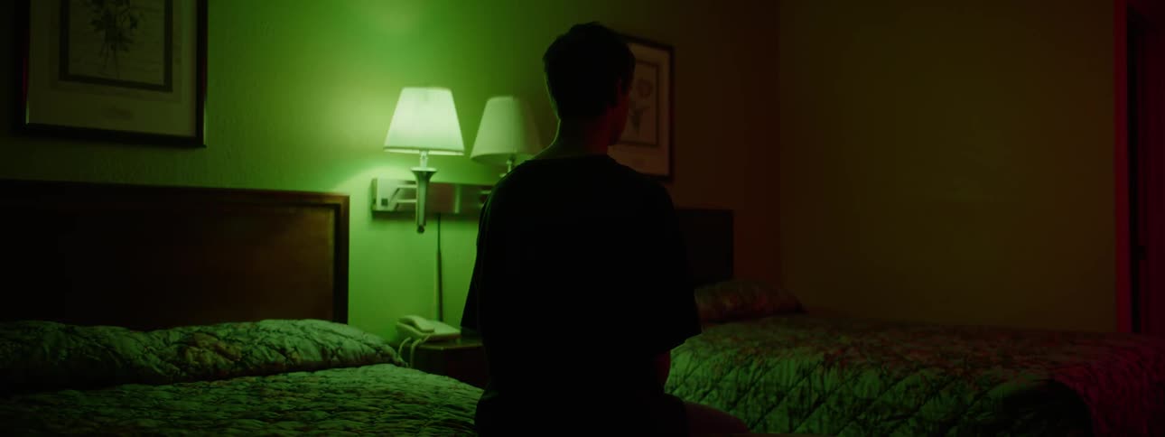 A young man is sitting on the edge of a bed in a hotel room