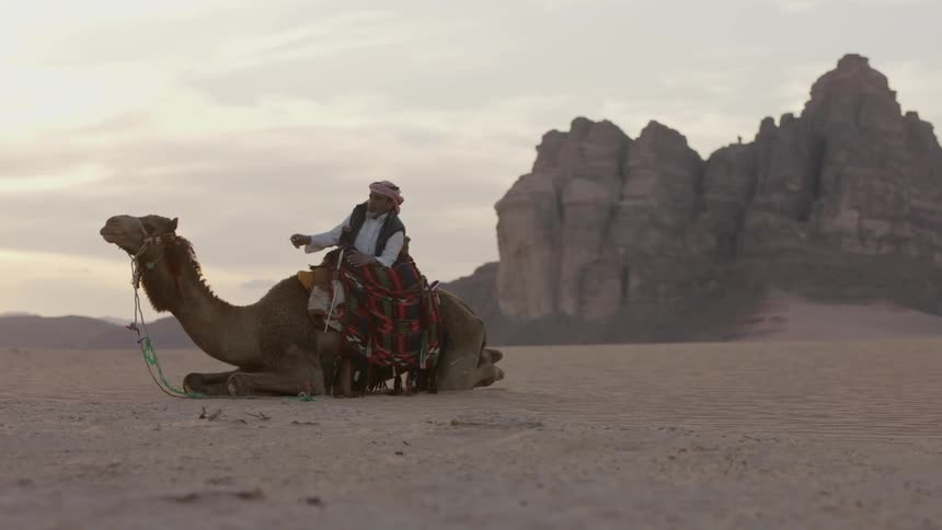 A man is sitting on a camel in the middle of the desert