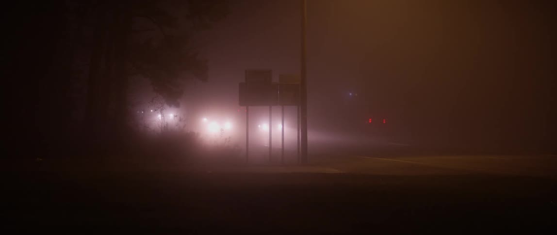 Vehicles travel down the foggy road at night
