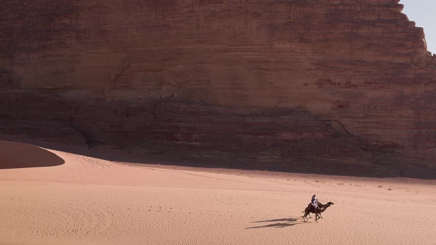 Two men ride camels across a desert