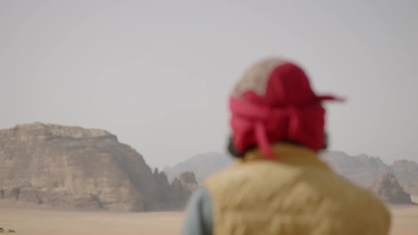 A man wearing a turban looks around in the desert