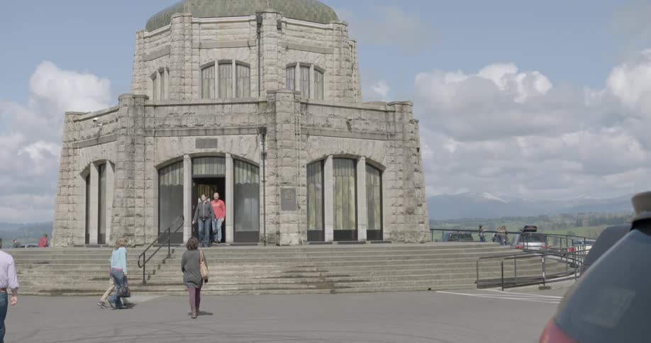 People walking towards a stone building overlooking the mountains
