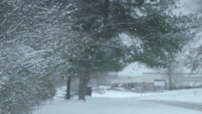 Snow falls as a car drives by
