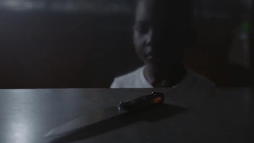 A boy looks at a knife on a kitchen counter