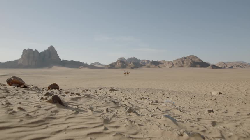 Two people ride camels in the desert