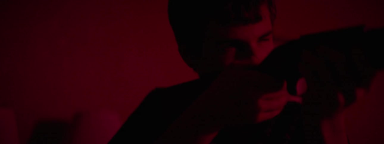 A teenage boy is aiming a rifle as he stands in a room