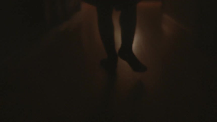 Someone is walking down a dark hallway barefoot on a hardwood floor
