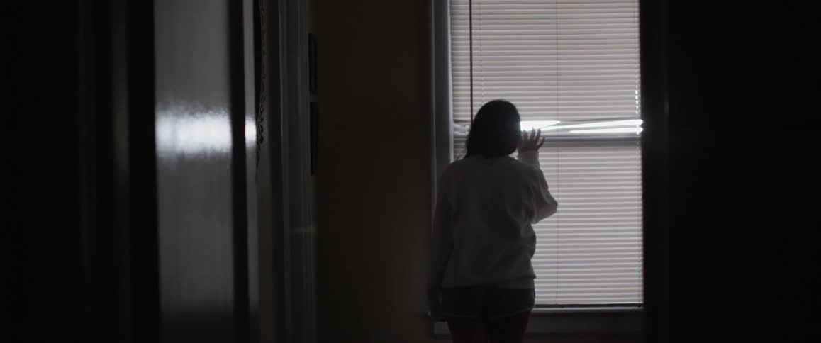 Woman creates an opening in the blinds and peeks outside