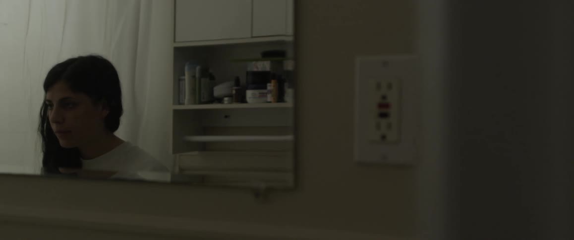 A woman is standing in the bathroom looking in the mirror