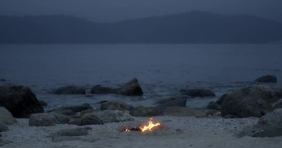 A small campfire is burning near the water