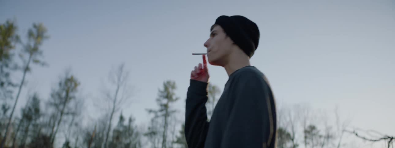 A teenager walks on a field smoking a cigarette