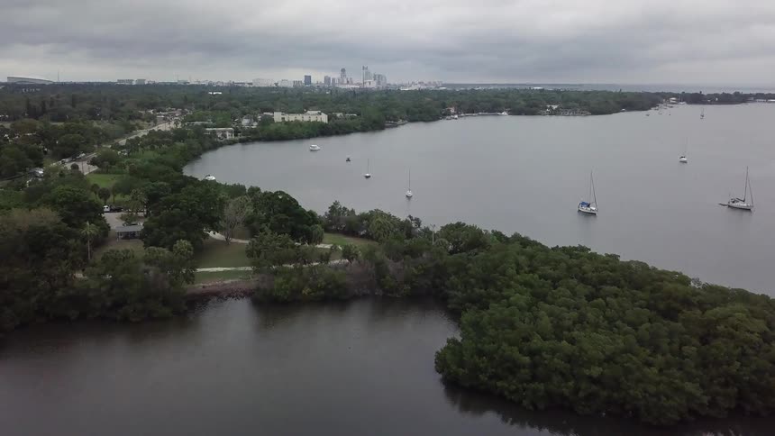 A large city is in the distance and a small suburb with fishing boats are being filmed from a drone