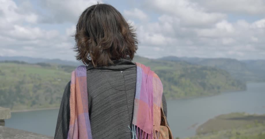 Woman is walking along the balcony and is looking at the river beneath