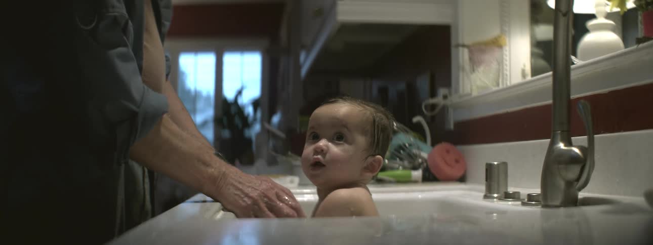 A parent is bathing a baby in the kitchen sink