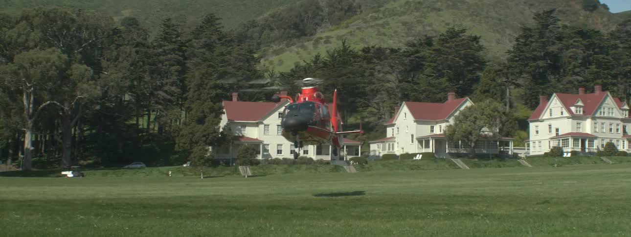 A orange helicopter is taking off from a field