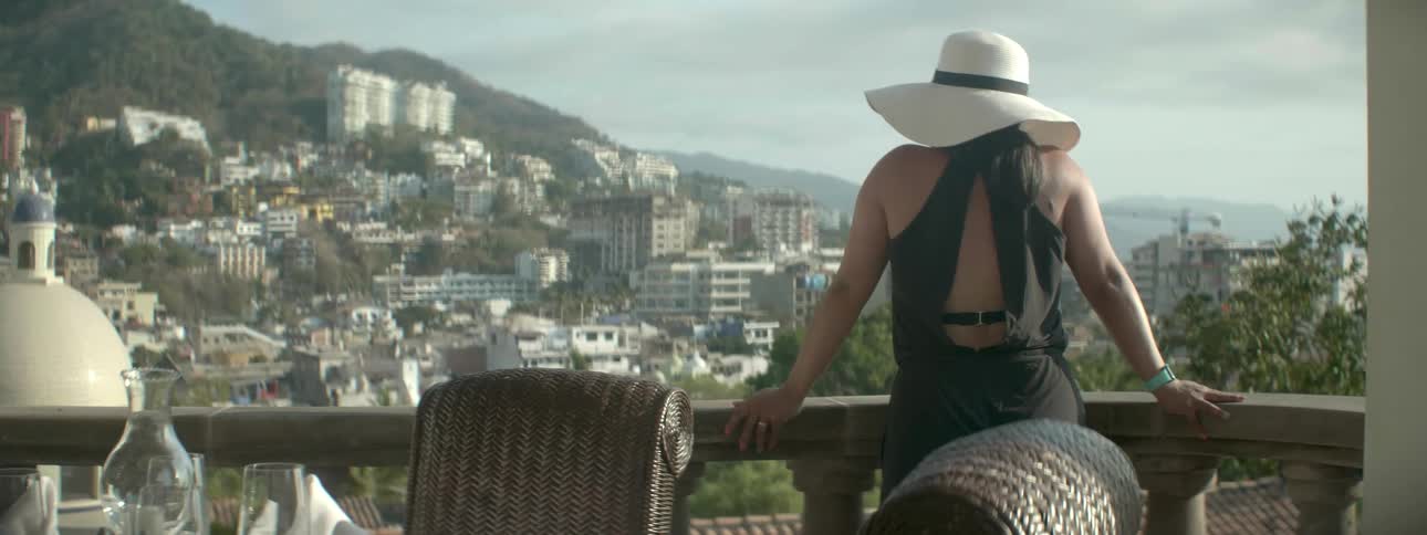 A woman walks onto a balcony and looks over the edge at the city