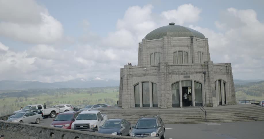 External view of Vista House observatory with cars parked outside and the mountains in the distance