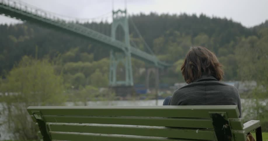 A lonely woman sitting on a bench by the bridge