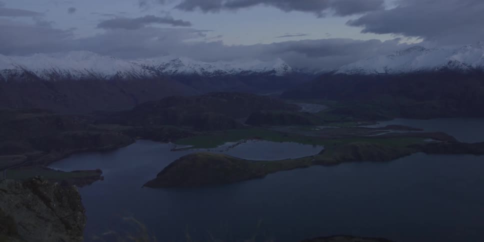A lake with grass in the foreground and mountains and the sky in the background