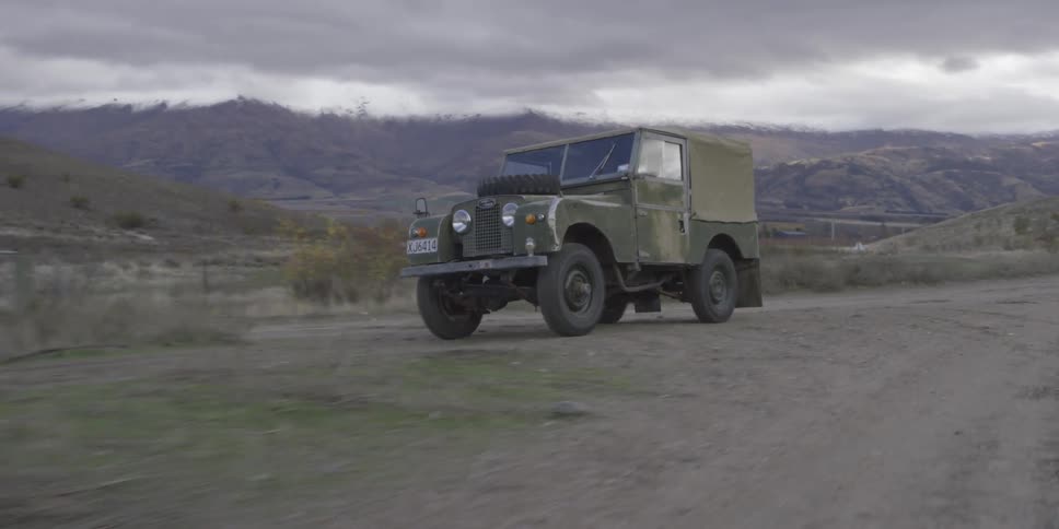 A green jeep drives down a dirt road near mountains