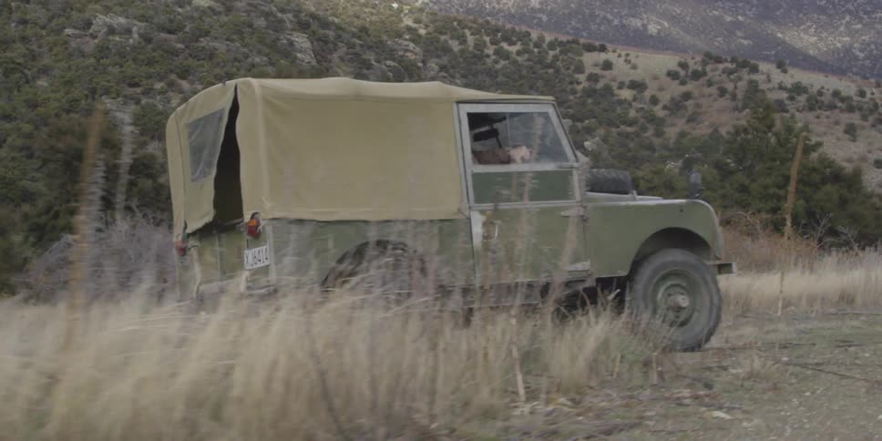 A covered jeep speeds recklessly along a dirt road in the mountains