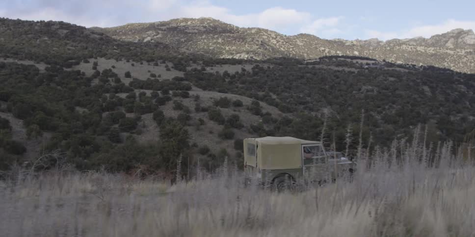 A green jeep drives down a dirt road near mountains