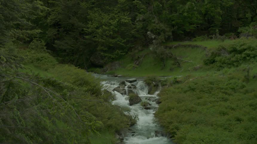 A small stream turns into a larger stream surrounded by green valleys