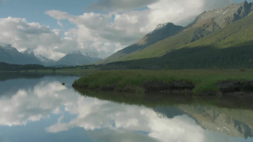 The water is calm along the shore of the mountain