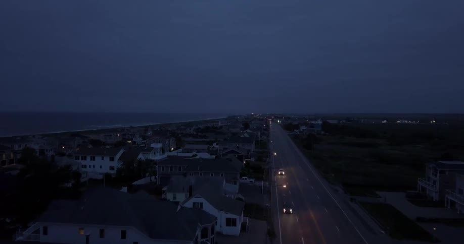 Cars with headlights on travel on a highway near homes