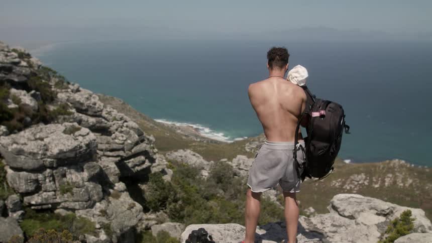 Man sets his camera and backpack down on a rock overlooking the ocean