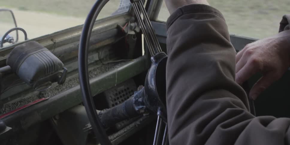 A bearded man drives an old truck down a bumpy road