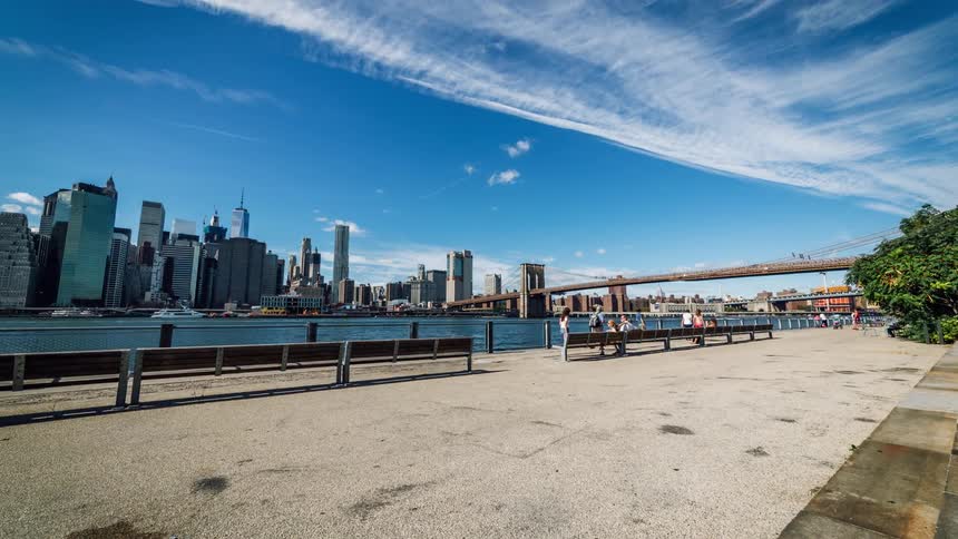 Timelapse of people walking on a sidewalk near a river and a city