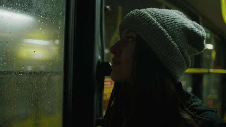 A woman riding on a train looks out the window at the passing traffic