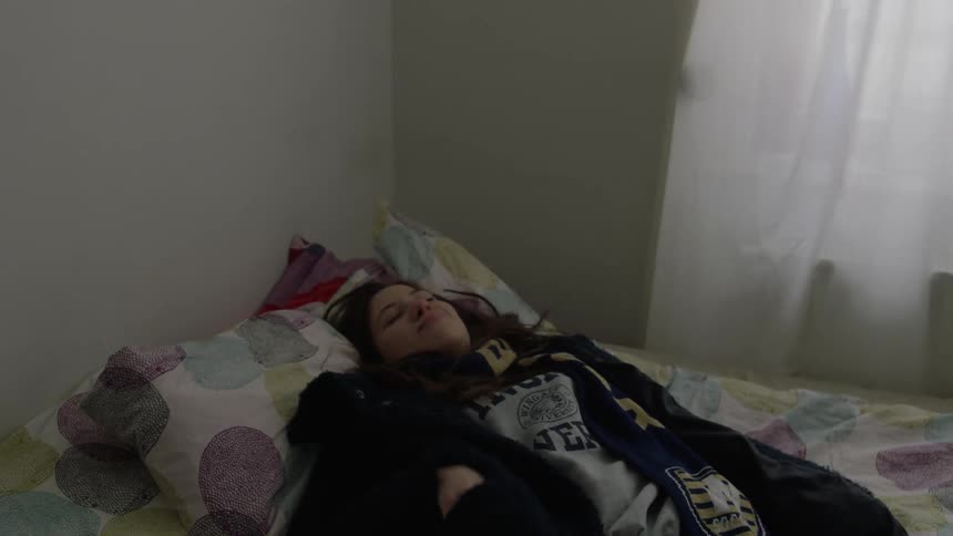 A woman lays down on a bed and looks at her phone