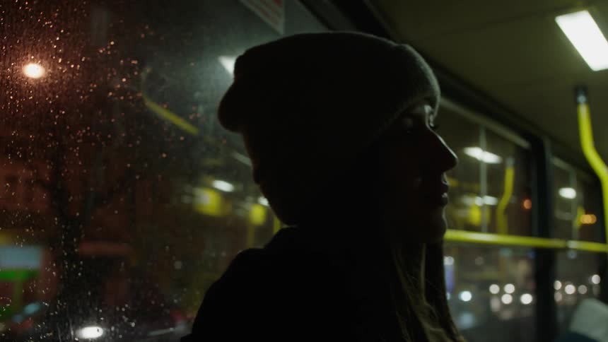 A woman travels on a train through the city at night