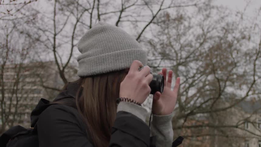Woman wearing a toque takes a picture outdoors with a camera