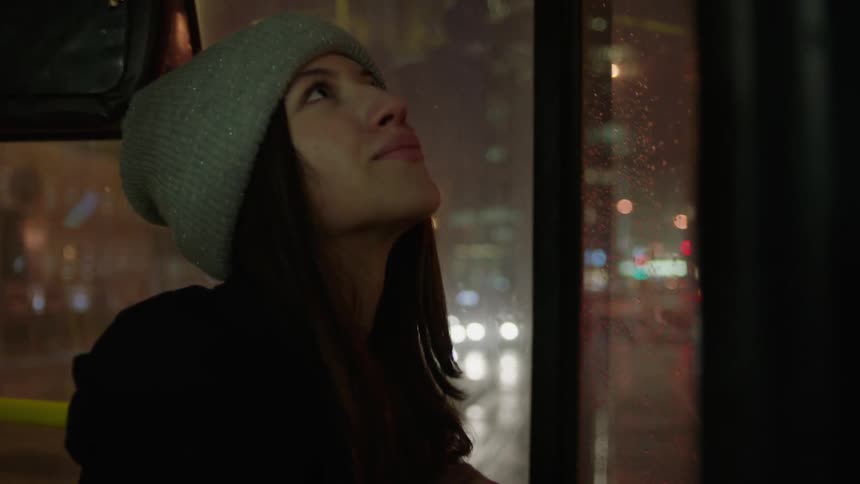 A woman smiles while looking out a bus window