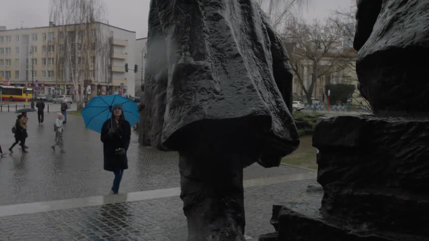 A woman carrying an umbrella walks near a monument on a rainy day
