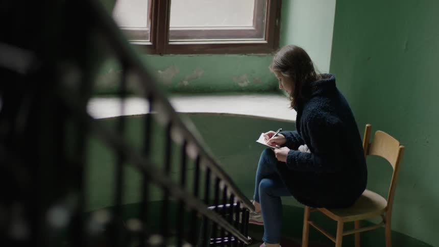 A woman writes in a book watching sitting by a window