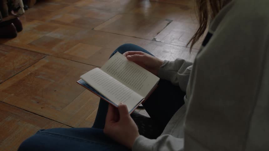 Person sits reading a book indoors on a sunny day