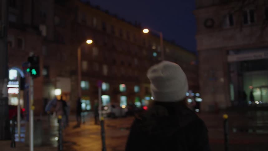 A woman is walking across a street in the city on a rainy night