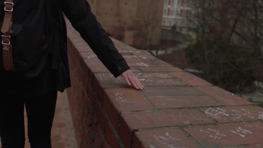 Woman walking over a bridge touching the brick ledge